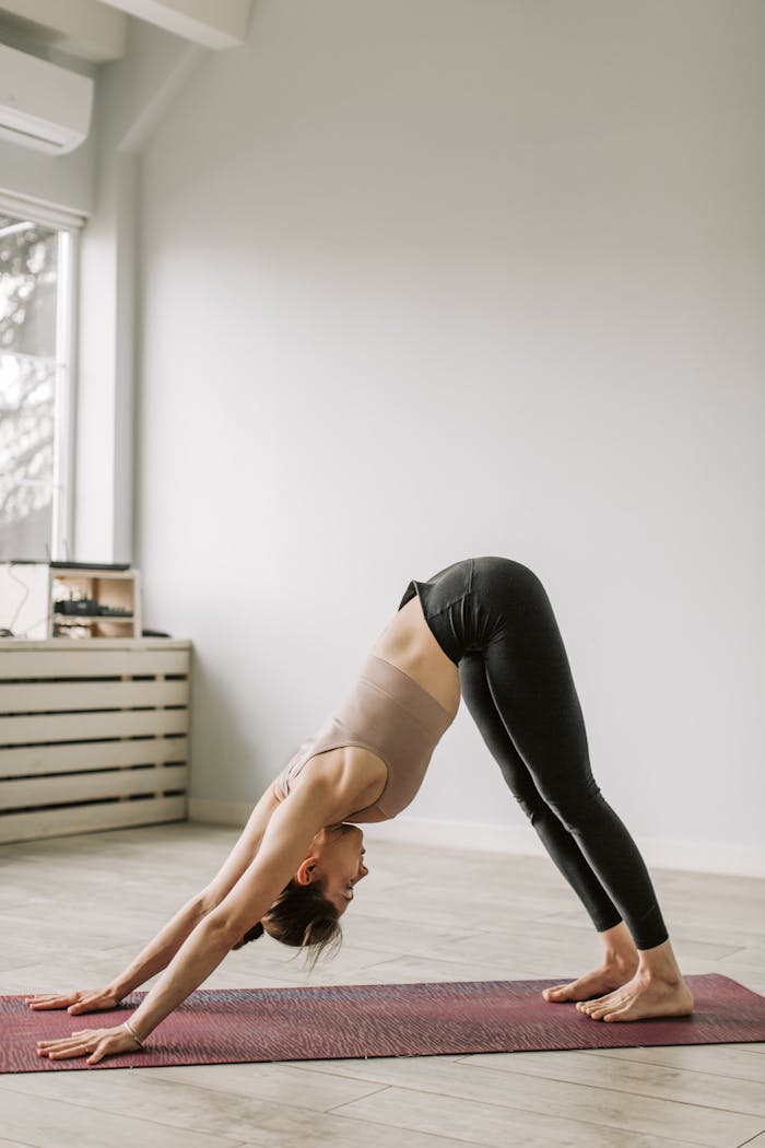 Home Adult woman in a downward facing dog yoga pose on a mat indoors during daytime.